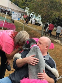 a man and woman hugging a poodle in a pink tutu